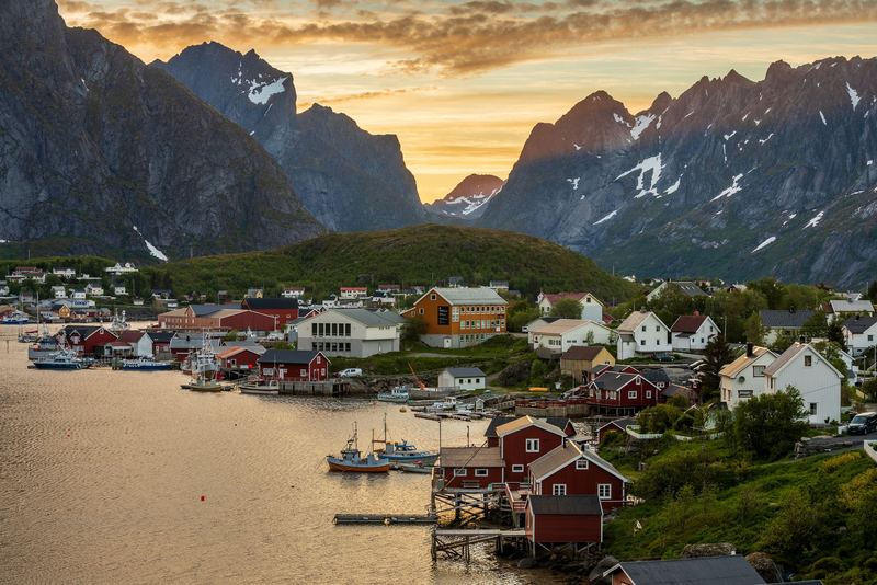 Red fishing cabins of Reine beneath jagged Lofoten peaks at dusk